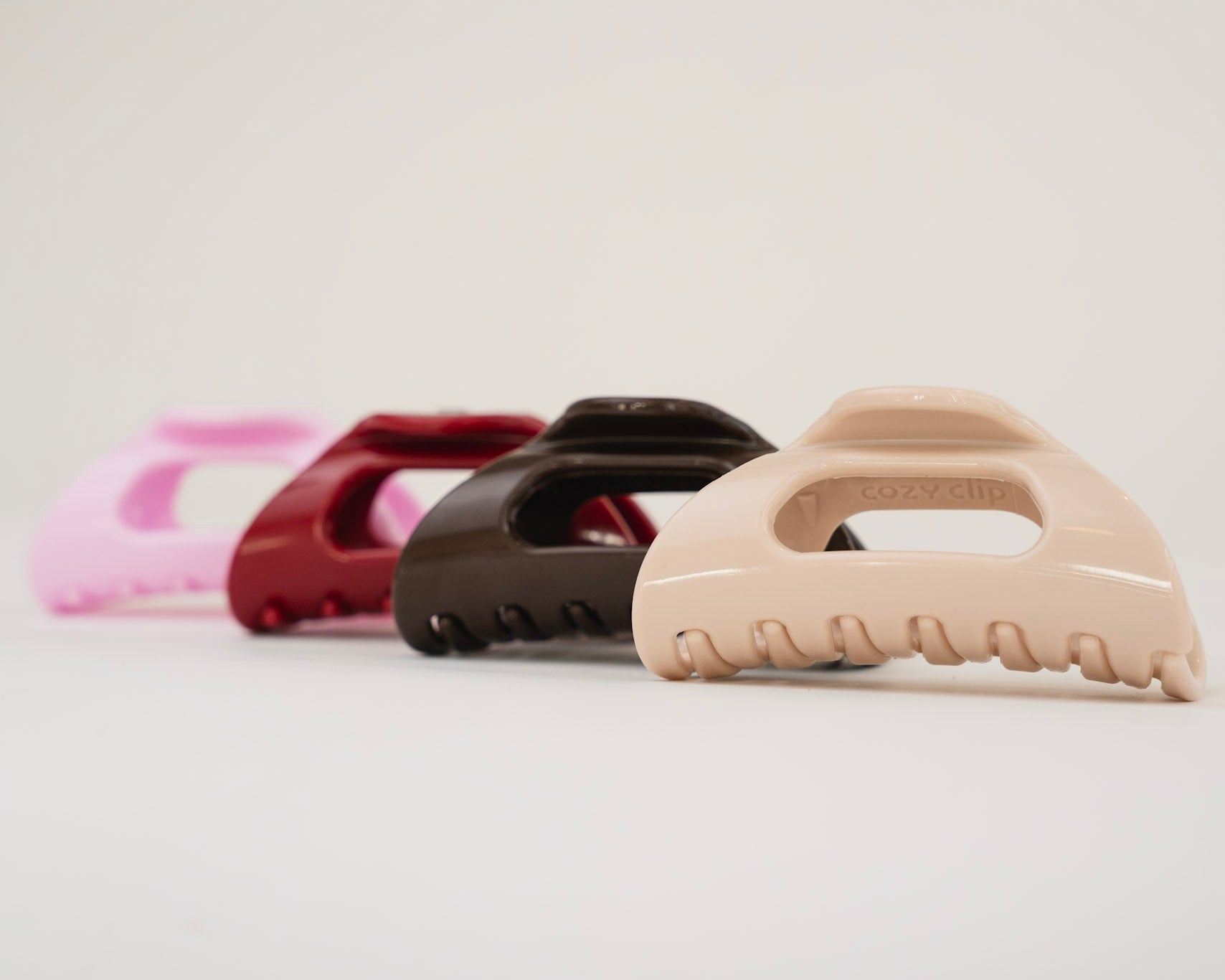 Cozy Clip® flexible claw clips in blonde, espresso, wine red, and baby pink; 'cozy clip' molded on the front blonde clip.