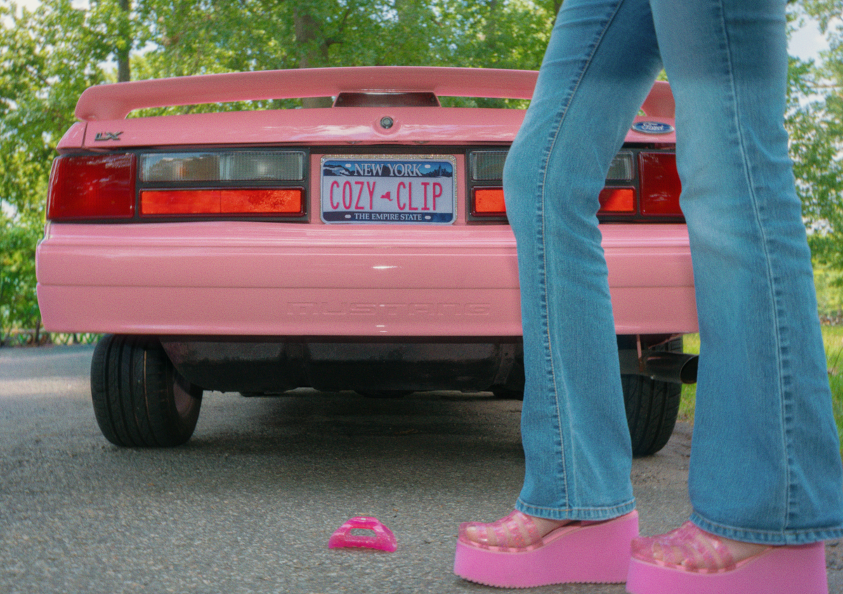 Glittery pink jelly flexible claw clip on pavement beside pink jelly platform sandals and a pink car