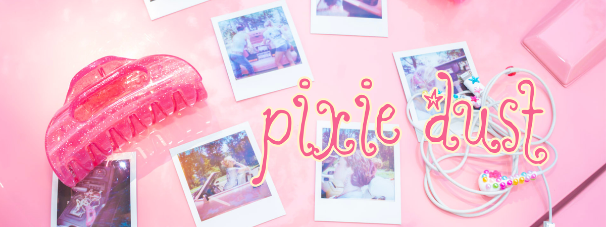 A pink flat-lay featuring a translucent pink hair claw clip, several Polaroid-style instant photos, white bedazzled earbuds, and decorative text reading 'pixie dust' on a pink background.